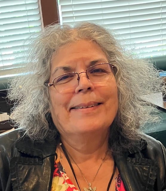 A smiling woman with glasses, gray hair, and a NarfOfficers badge.