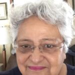 A smiling elderly woman with gray hair and glasses taking a selfie.